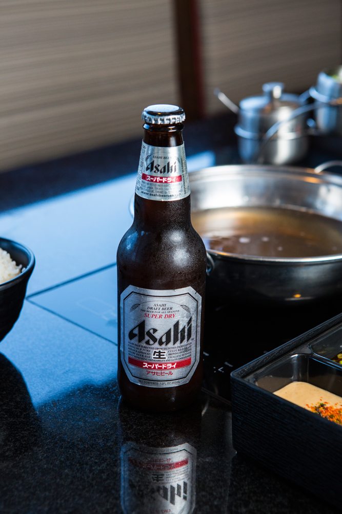 Small bottle of Ashai Super Dry beer in front of a beef broth pot.